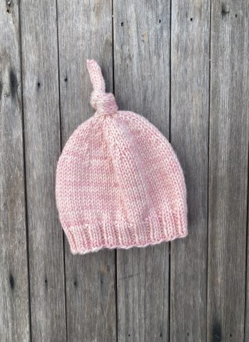 Pink knit newborn baby hat with knot on top on a wood background