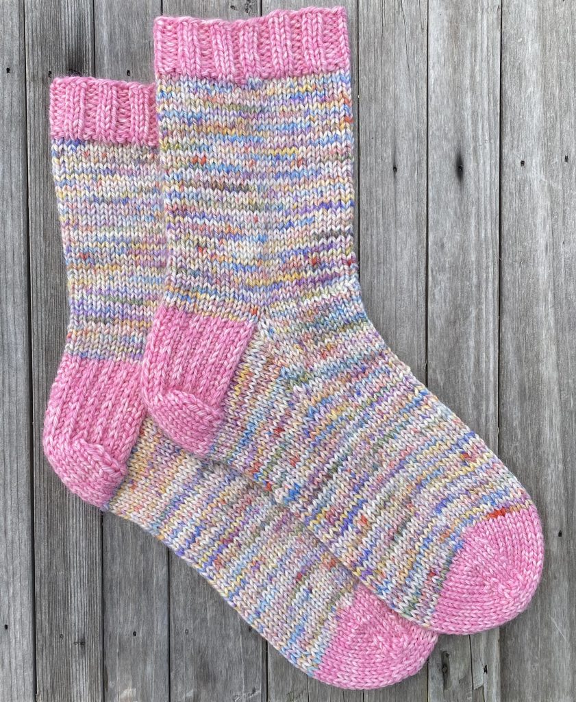 pair of knit dk socks in drops fiesta dk yarn color fairytale and strawberry ice cream on wood background