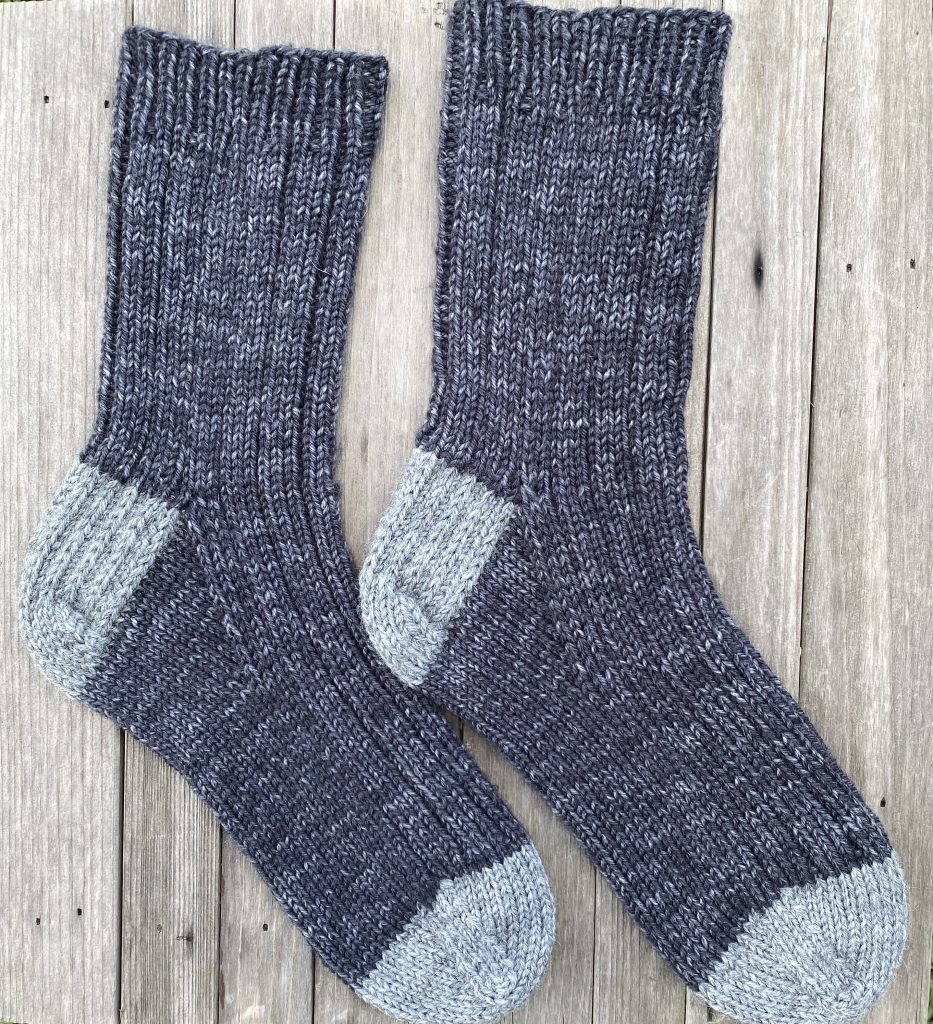 pair of gray mens socks hand knit in drops fiesta yarn on wood slat background
